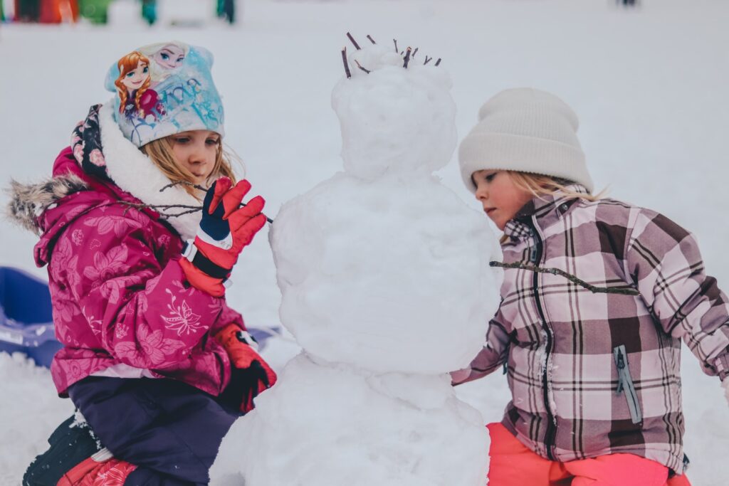 two girl molding a snowman during daytime as a fun January activity.